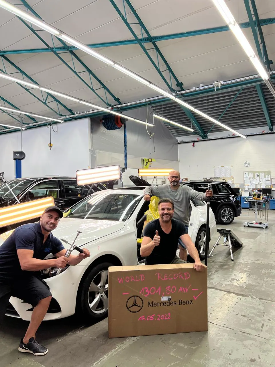 Team nach Abschluss einer außergewöhnlich umfangreichen Hagelschadenreparatur an einem Mercedes-Benz, davor ein Karton mit der Aufschrift 1301,80 AW
